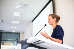 Female academic speaking from a podium delivers a conference 