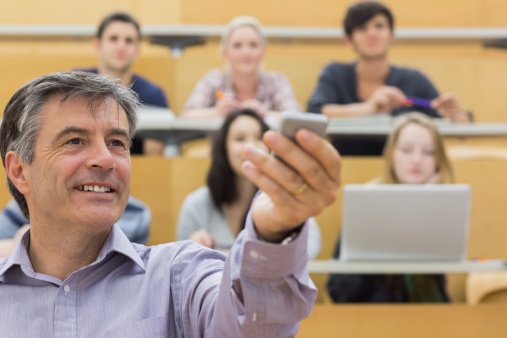 Lecturer holds up presentation clicker in the presence of his students 
